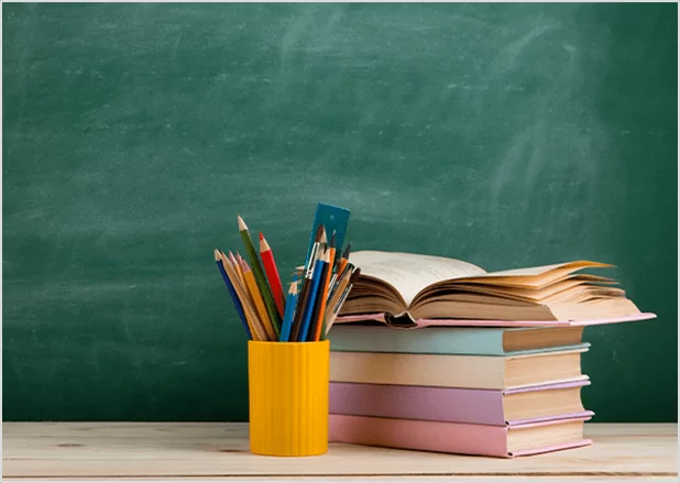 Stack of books and pencils in front of a chalkboard, highlighting comprehensive educational publishing services.