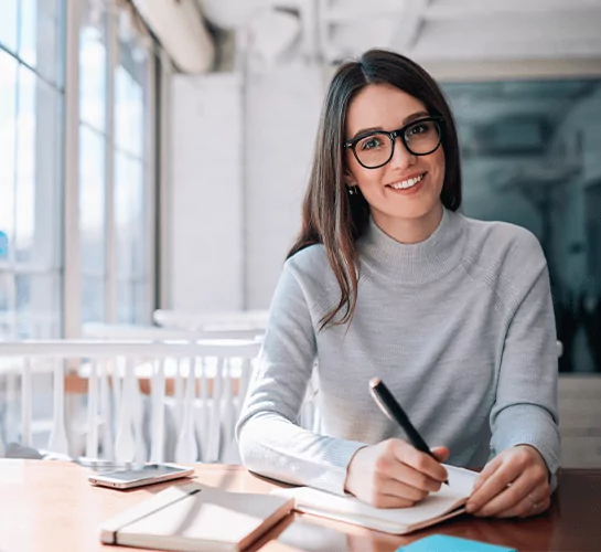 A smiling female author writing in a notebook, showcasing creative writing services and author support.