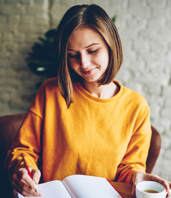 A young creative author at Prestige Publishings writing in a journal with a cup of tea.
