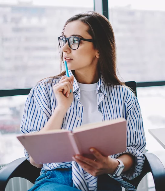 A thoughtful young woman with glasses and a striped shirt holding an open book, representing expert literary consulting and creative development.