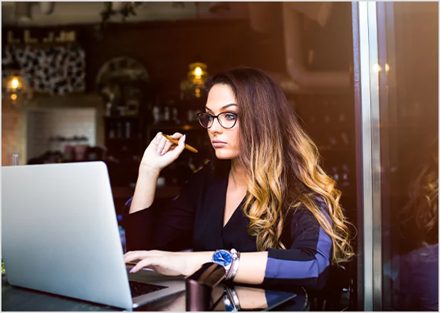 A focused woman with glasses working on a laptop in a cafe, representing professional manuscript editing and author services.