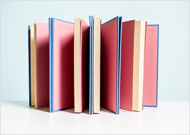 A group of hardcover books with blue spines and pink pages standing vertically in a circular arrangement, representing high-volume bulk publishing and premium book binding services.