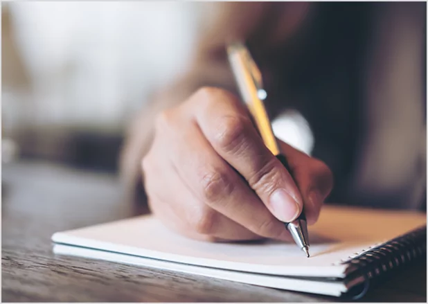 Close-up of a hand holding a pen and writing in a notebook, symbolizing dedicated author support and storytelling.