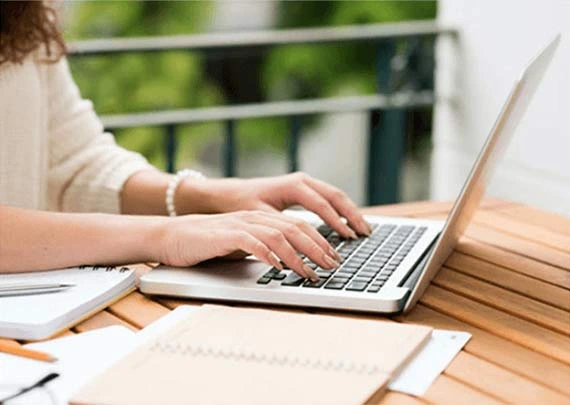 A person typing on a laptop at a wooden table, representing professional ghostwriting and book editing services.
