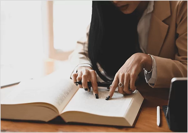 A woman in a tan blazer pointing at text in a large open book, illustrating professional legal publishing and detailed manuscript fact-checking services.
