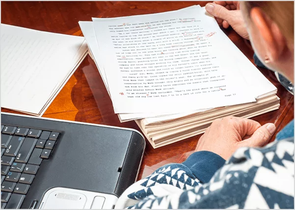 An editor reviewing a printed manuscript with red ink marks, illustrating professional book editing and proofreading services.