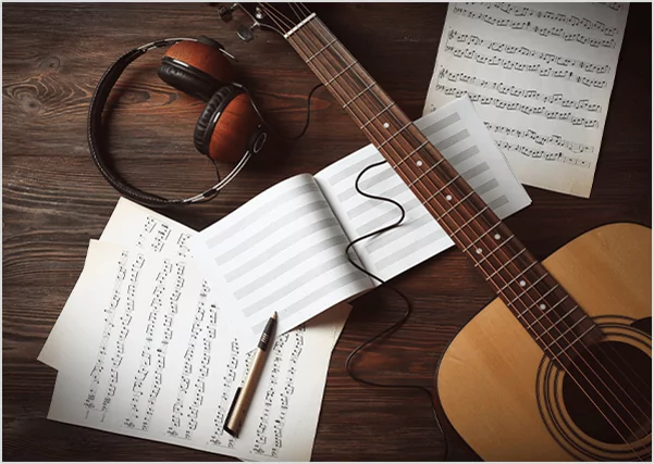 Acoustic guitar with headphones and sheet music on a wooden desk, representing professional music publishing and songwriting services.