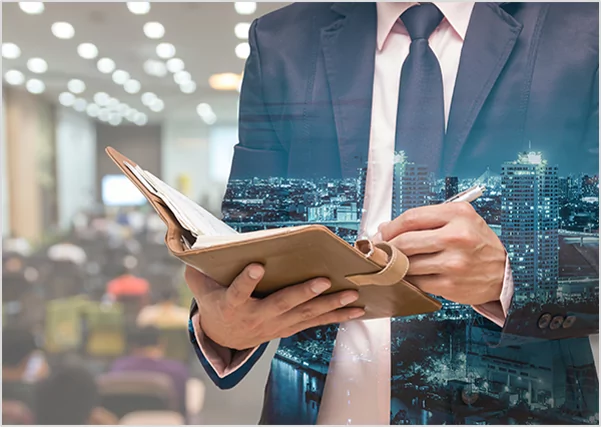 : Double exposure image of a businessman in a suit writing in a leather planner, overlaid with a glowing nighttime cityscape, representing corporate strategic planning and urban business development.