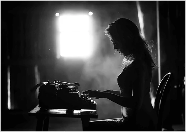 Silhouette of a woman typing on a vintage typewriter in a dimly lit room with a bright window, representing classic professional storytelling and manuscript typing services.