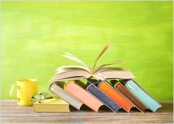 An open book resting on a row of colorful slanted books next to a yellow mug, representing vibrant creative book design and publishing services.