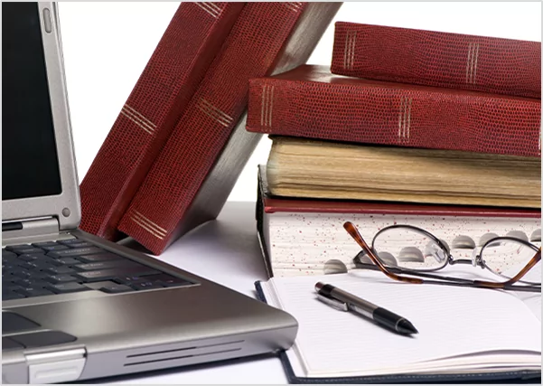 Laptop, reading glasses, and an open notebook next to a stack of vintage books, representing academic research and scholarly publishing services.
